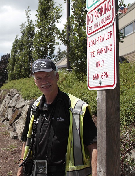 Bainbridge Island Parking Enforcement Officer Ken Lundgren stands with a sign reserving certain spaces downtown for boat and trailer parking. The unavailable spots upset some drivers