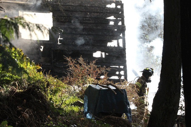 A Bainbridge firefighter walks past a burning home on the island's north end after emergency workers responded Sunday to a two-alarm fire.