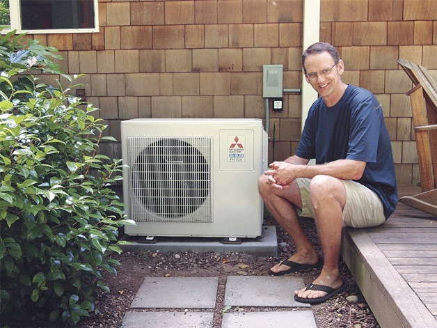 Chris McMasters sits next to his new energy-efficient heating system that replaced his home’s electric and propane heat. It is one of many upgrades he made to his 30-year-old house to make it more sustainable while cutting down on energy costs.