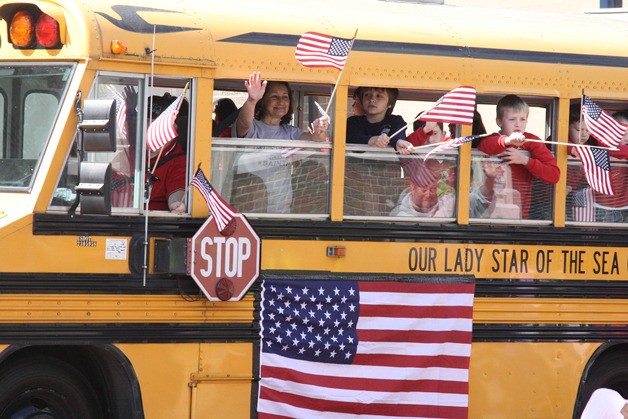 Students in a previous parade wave the U.S. flag from their school bus. Posting the U.S. flag during parades is an acceptable use of the flag.
