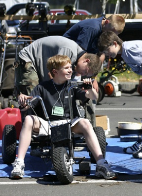 Blake Stephenson (seated) revs the motor while a trio of friends tune a three-wheeled go-cart at the Rotary Auction site at Woodward Middle School Monday. Volunteers are sorting