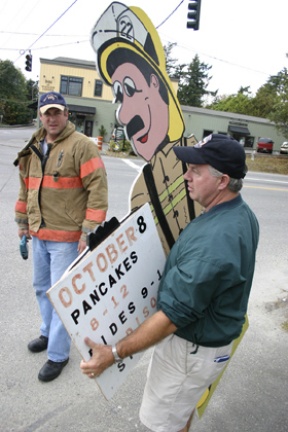 Firefighters Dave Hannon and Dave Coatsworth (background) take down a sign promoting the upcoming community pancake feed sponsored by the fire department. The signs had been tacked to utility poles at Winslow Way/305 and several other locations