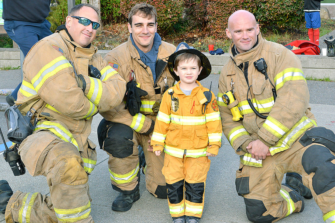 Young resident Owen gets to stand with firefighters Tony Parker, Justin Foley and Josh Foley at the Bainbridge Fire Department pancake breakfast on Oct. 14. (Mark Krulish/Kitsap News Group)