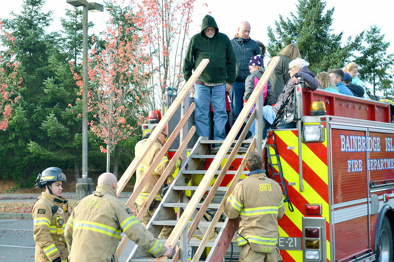 Firefighters help residents get on and off the top of the truck. (Mark Krulish/Kitsap News Group)