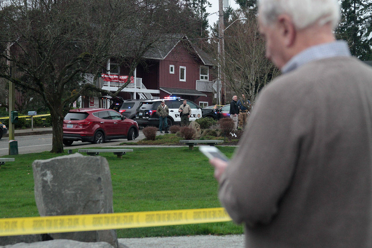 A bystander looks at his cellphone as police investigate an officer-involved shooting Wednesday afternoon near Winslow Green. (Luciano Marano | Bainbridge Island Review)