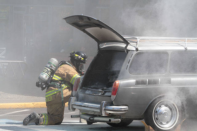 A Bainbridge Island firefighter kneels next to a Volkswagen Squareback station wagon that caught fire Monday in the parking lot of the Island Village Shopping Center. (Brian Kelly | Bainbridge Island Review)