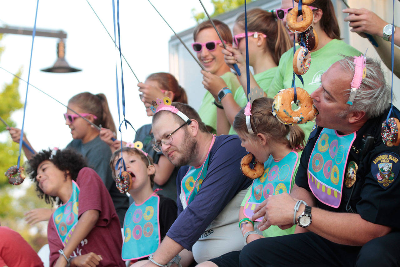 Islanders compete against Police Chief Matthew Hamner (far right) in the doughnut-eating contest at last year’s National Night Out. (Luciano Marano | Bainbridge Island Review)