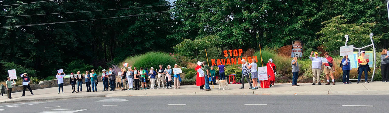 Demonstrators at the #StopKavanaugh protest at Waypoint Park hold up signs to motorists passing through downtown Winslow on Aug. 16. (Ricann Block photo)