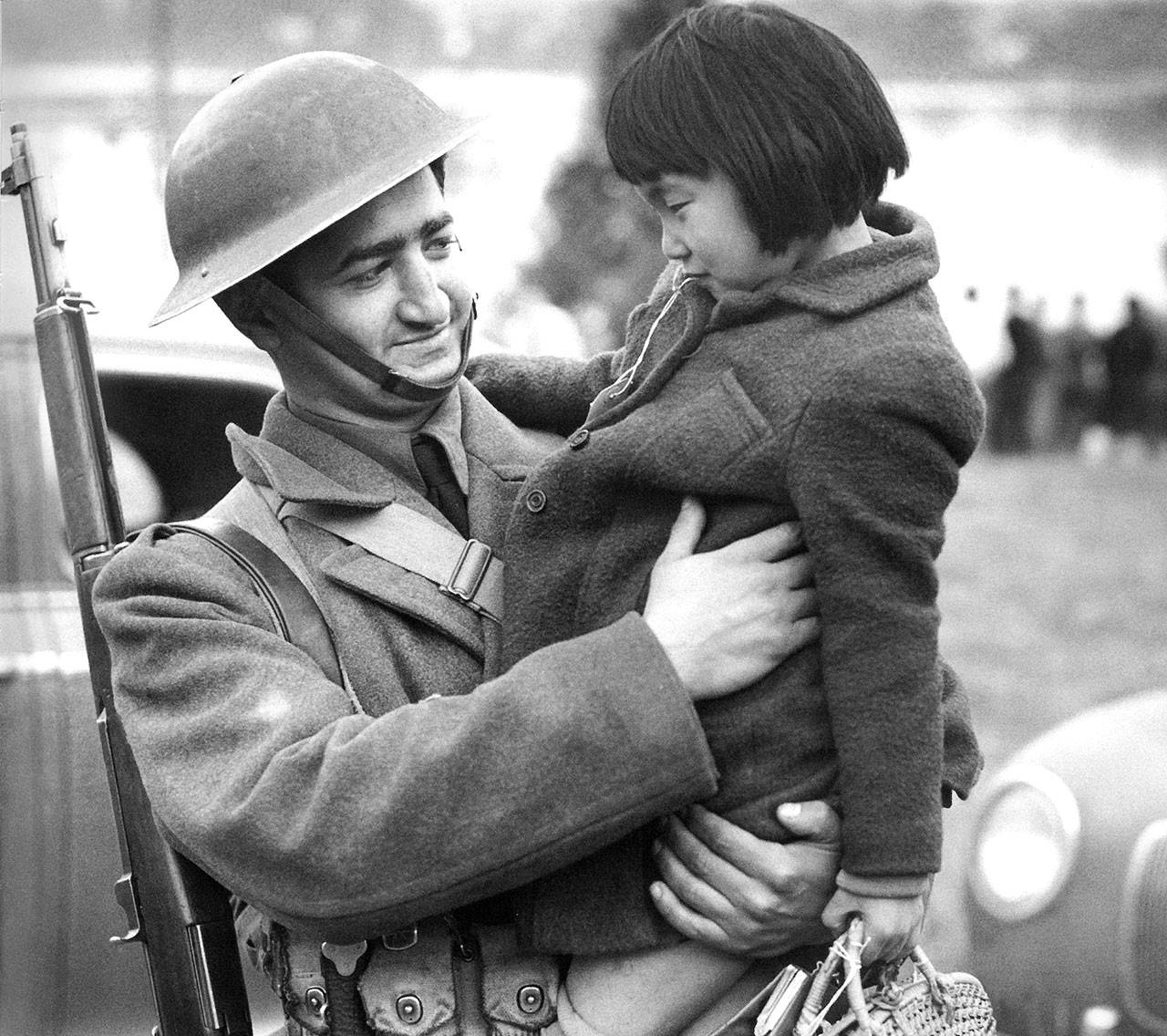 An Army soldier holds Setsuko Kino, 8, while they wait for the ferry Kehloken to arrive to take Japanese American families off Bainbridge Island on March 30, 1942. (Photo courtesy of the Bainbridge Island Historical Museum)