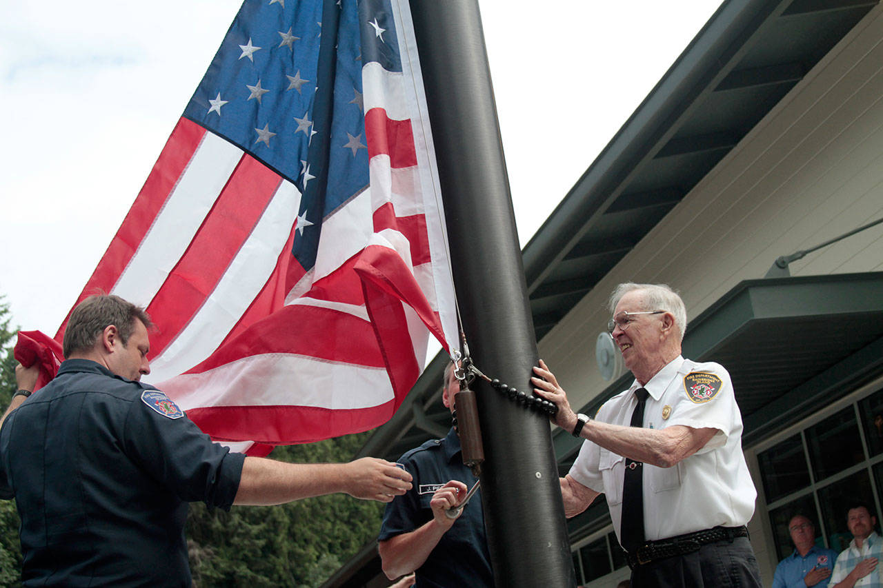 Luciano Marano | Bainbridge Island Review - Bainbridge Island Fire Department Assistant Chief Chuck Callaham (right), who has been with the department, serving in various capacities, since 1951, conducted the inaugural flag raising at the newly rebuilt Station 22 Monday, Aug. 12.