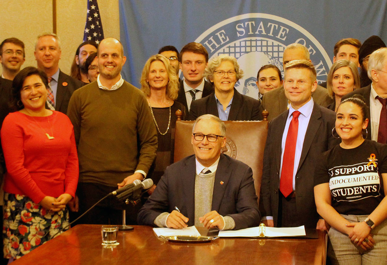 Gov. Jay Inslee, seated, signs the first bill of the 2020 legislative session into law. On the right stands the bill’s primary sponsor, Sen. Jamie Pedersen, D-Seattle, who is wearing a red tie. (Cameron Sheppard | WNPA News Service)