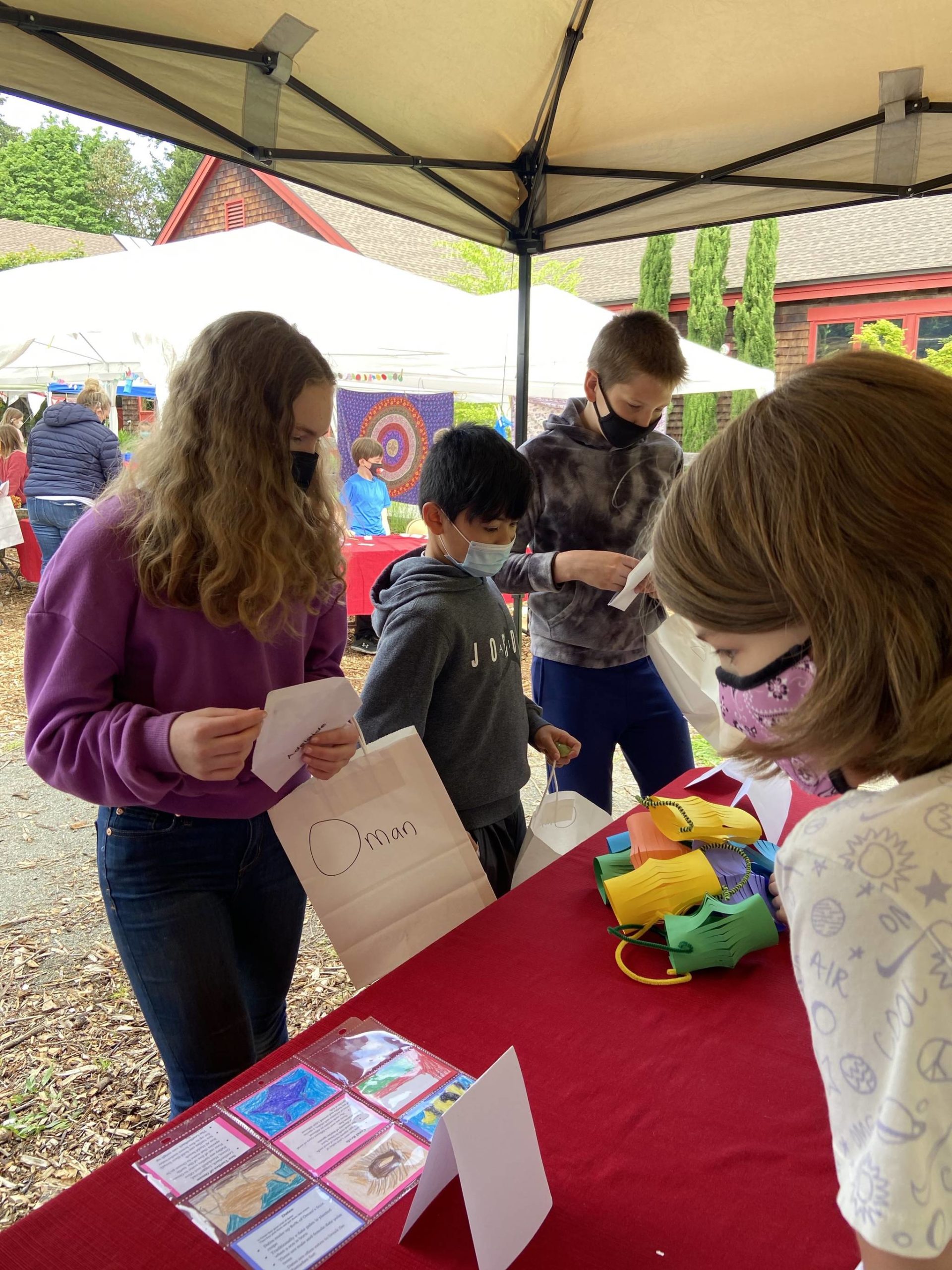 Fifth graders Adelaide Scott, 11, Cruz Garcia, 10, and Dylan MacCulloch, 11, admire the paper lanterns and handmade trading cards offered by Liviana Lannon Eatinger, 8.