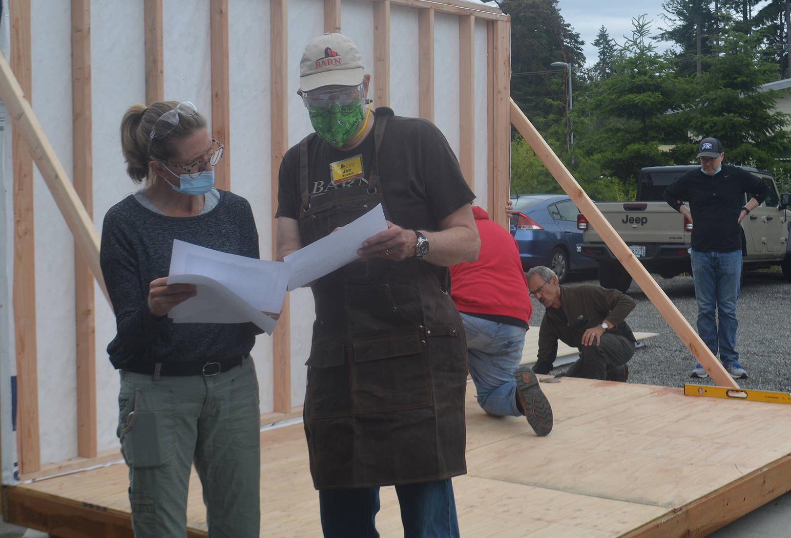 Volunteer Tammy Galbraith and “Stretch” go over the floor plans for the tiny house as volunteers put up one side of the house in the background.
