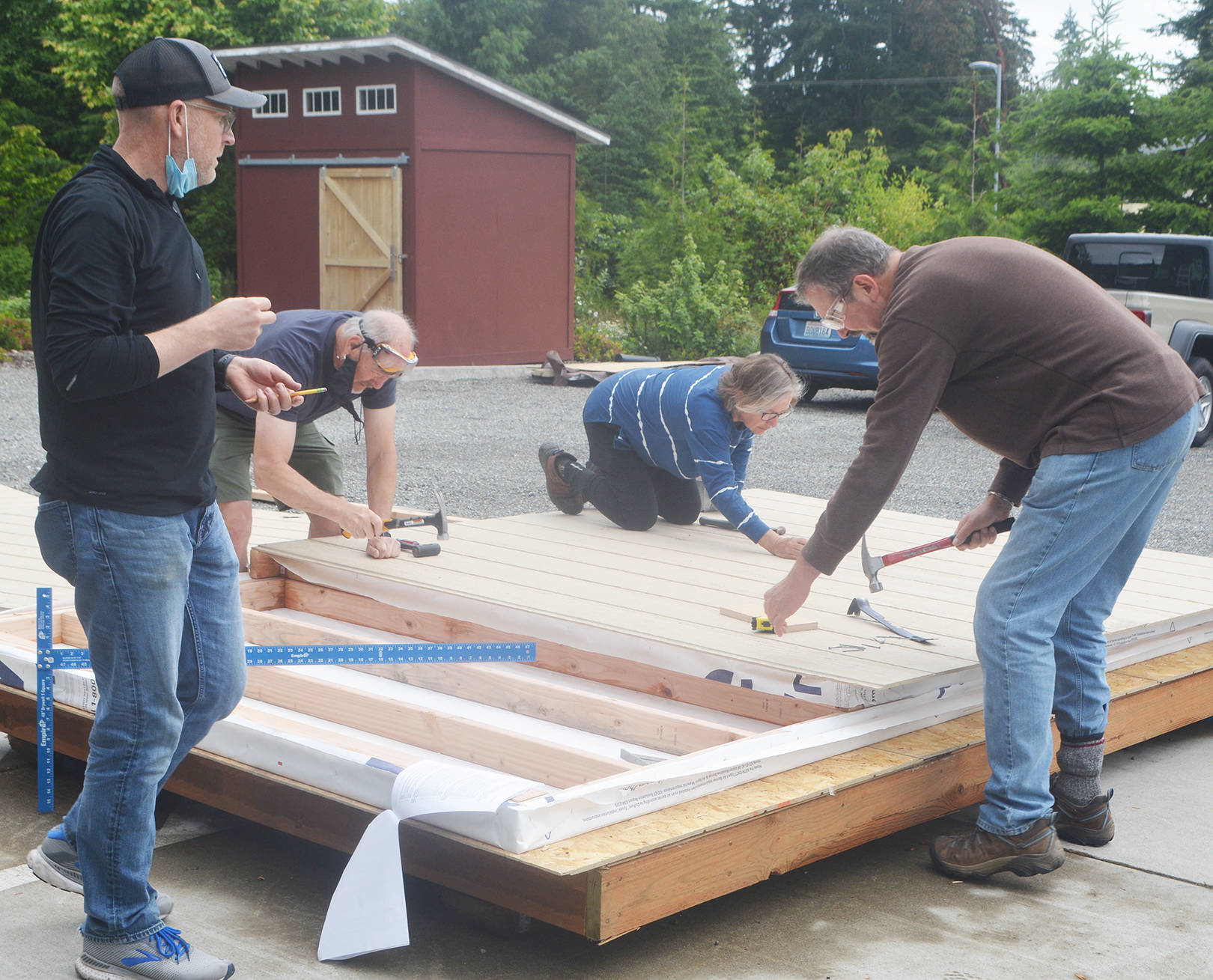 Volunteers nail siding onto the frame of one of the walls of the tiny house.