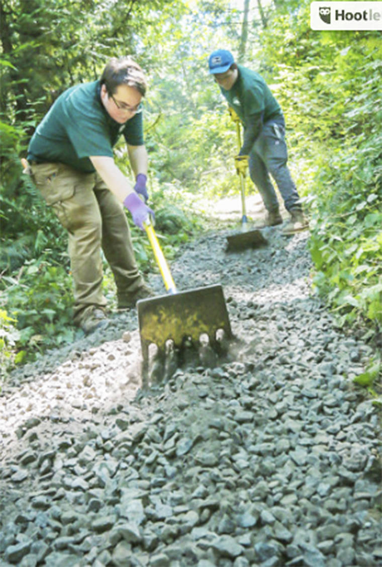 Benjamin Logan uses a rake to level out rocks on a trail.