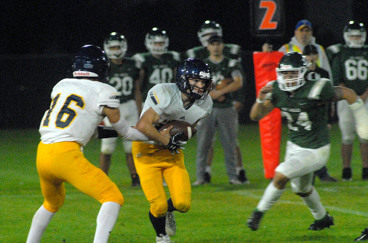Bainbridge quarterback Jack Grant, left, hands off to Garrett Goade as Port Angeles defender Jeremiah Hall closes in on Friday night in Port Angeles. (Keith Thorpe/Olympic Peninsula News Group)