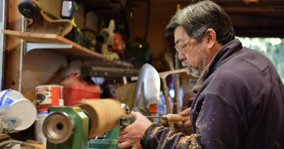 Carpenter Mike Okano shapes a kine from a cherry wood log on his lathe.