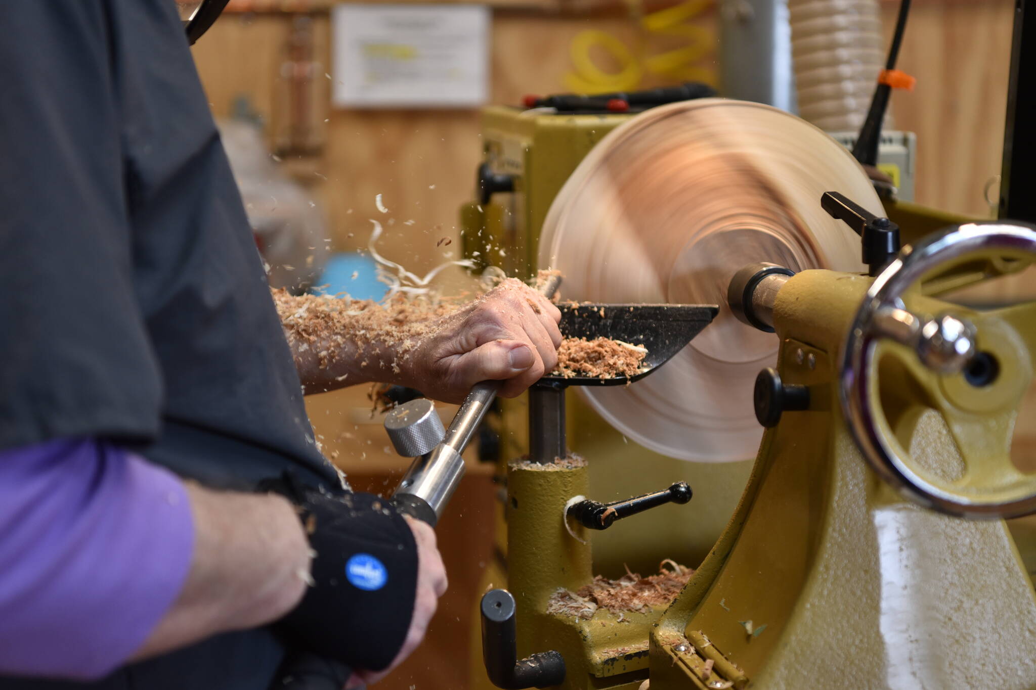Wood shavings fly as a BARN member carves using a lathe in the wood shop.