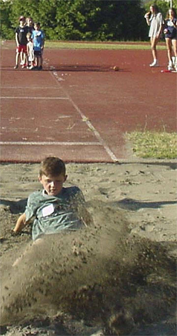 A boy kicks up a bunch of sand in the long jump.