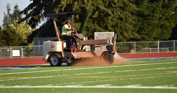 Coast to Coast turf employee, Roperto Salinas, drives a large power broom brushing the infill into the new turf at BHS Memorial Field ensuring a uniform placement to help prevent injuries to student-athletes. Nancy Treder/Bainbridge Island Review Photos