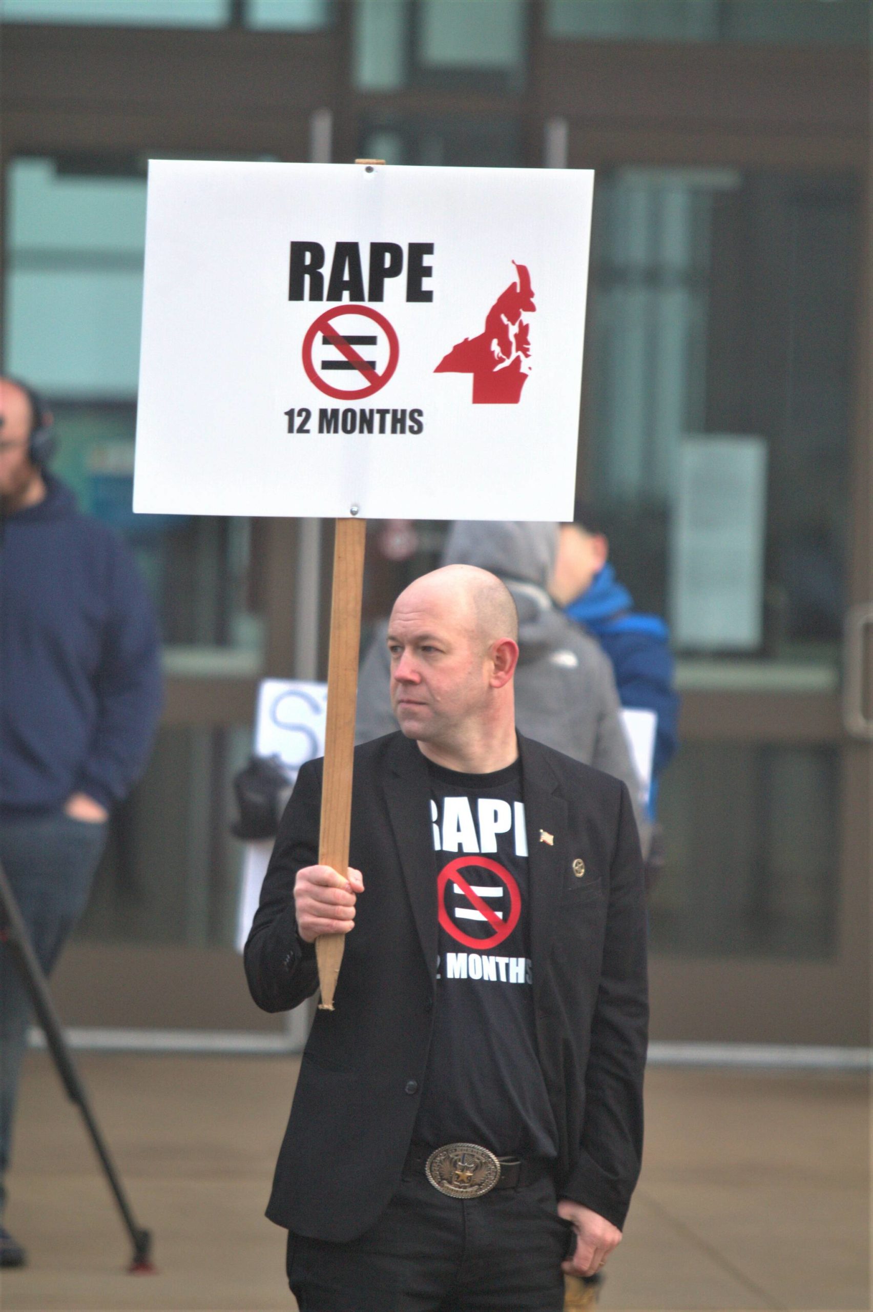 Local politician Rick Kuss holds a sign with the same message as his recently marketed shirt in protest of the plea agreement in a rape case.