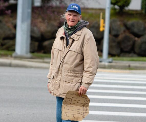 <p>A man stands on the curb nearby Bremerton’s Fred Meyer asking for cash from passing cars. Elisha Meyer/Kitsap News Group</p>