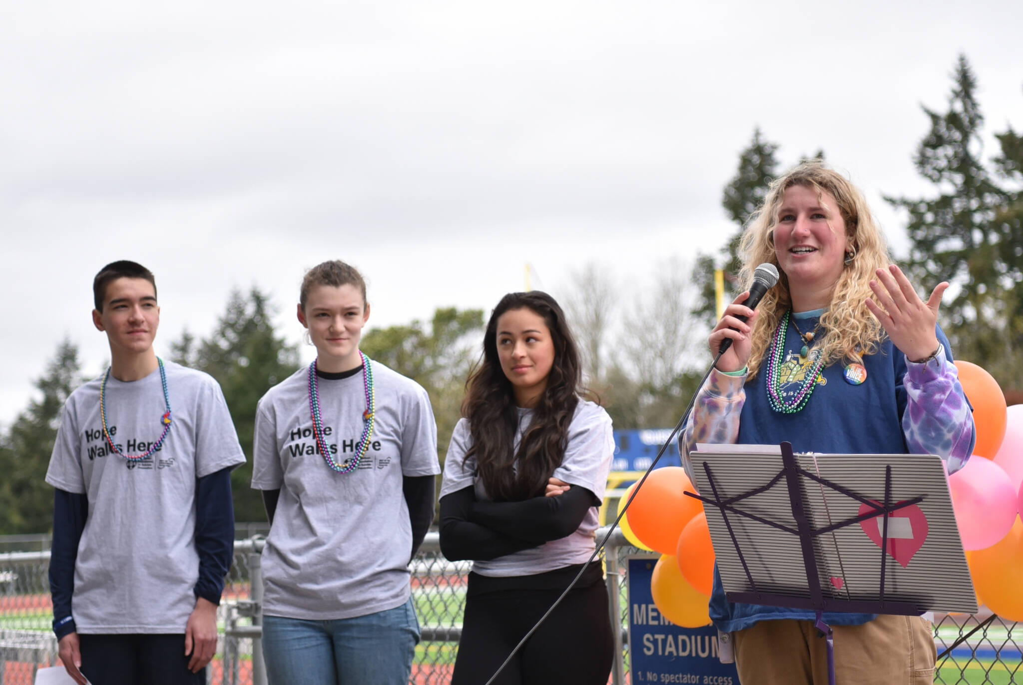 Sophomores Theo Oestreich, Maia Greiwe and Mae Wysong look on as Alexandra Velisaris speaks to attendees before the walk began.