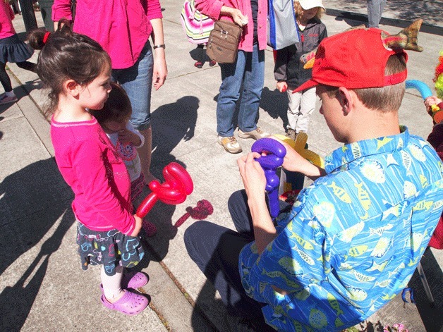 A young girl waits for a balloon bender to finish making a sword so she can battle the crowd at the popular Bainbridge Island Farmers Market.