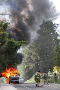 Bainbridge Island firefighters unroll hoses as they prepare to douse a vehicle fire Tuesday on Wyatt Way near the Grow development.