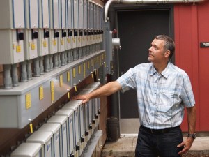 Joe Deets looks over the line of inverters that now scale the rear wall of city hall’s council chambers. The inverters turn the direct current of electricity from the solar panels into alternating current that the building can use.