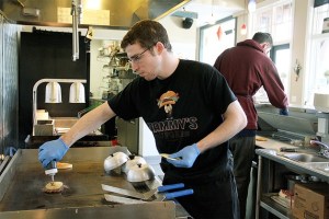 Corey Dunn doctors up a Hawaiian burger while Hammy’s co-worker Adam Bradford preps another burger in the back.