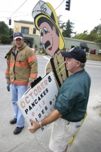 Firefighters Dave Hannon and Dave Coatsworth (background) take down a sign promoting the upcoming community pancake feed sponsored by the fire department. The signs had been tacked to utility poles at Winslow Way/305 and several other locations