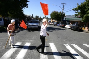 Senior center members Ruth Wender (left) and Dorothy Bland take crosswalk flags on their first journey across Winslow Way. The flags are part of a new pilot project to improve pedestrian safety.