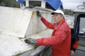 Mike Rose of the Bainbridge Harbor Commission helps secure a derelict vessel on Eagle Harbor during impound by the police Friday morning. The vessel was moved to a secure moorage to await disposal.