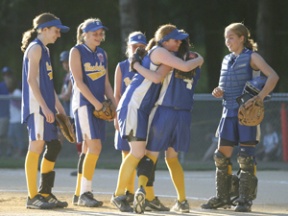 First baseman Grace Campbell embraces third baseman Delcy Stoddard after Stoddard scored the run to tie the girls’ Little League Juniors All-Star district game in the sixth inning Sunday at Strawberry Field. From left to right: Clara Dunn