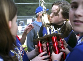 Kelsey Isenman (top) of the Diamonds gives the team’s new trophy a kiss after they defeated the Commotion 4-1 at Wednesday’s Little League Majors softball championship game. It was the second straight year the Diamonds won the title.