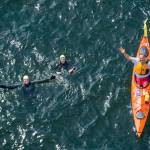 Photo courtesy of Pete Saloutos.                                Heather Burger, Kymmberly Myrick and Cris Ugles wave as they cross beneath the Agate Pass Bridge during Arms Around Bainbridge&rsquo;s round-the-island relay swim in 2013.
