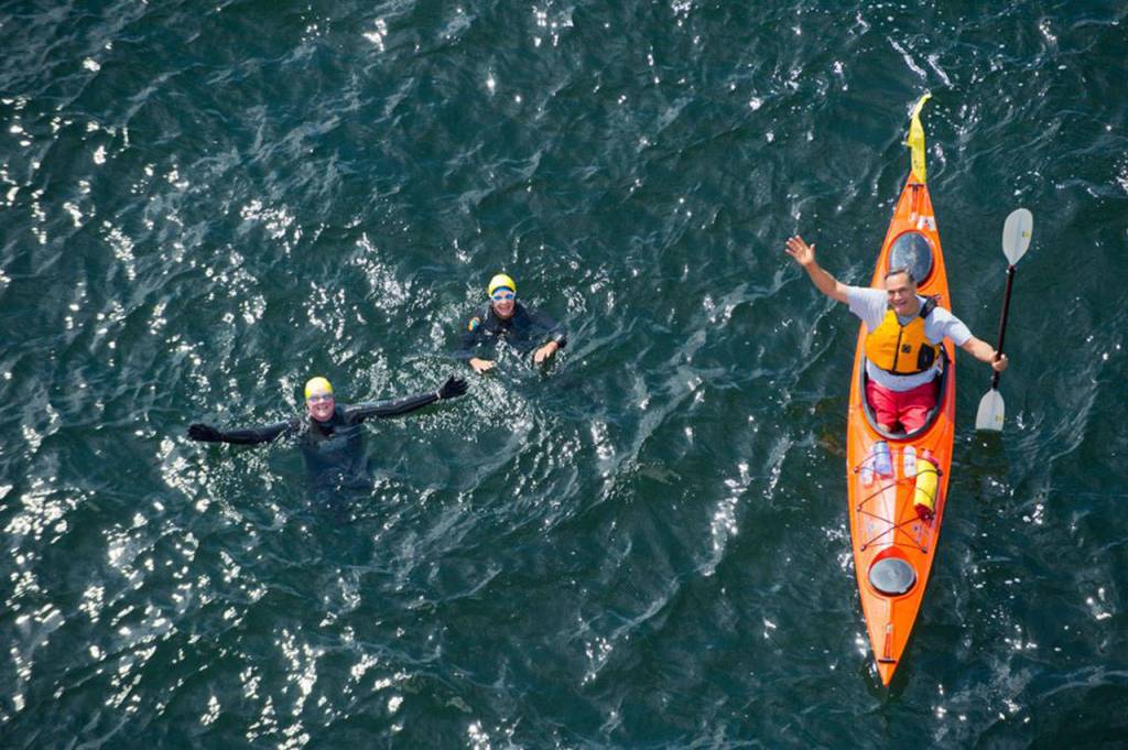 Photo courtesy of Pete Saloutos.                                Heather Burger, Kymmberly Myrick and Cris Ugles wave as they cross beneath the Agate Pass Bridge during Arms Around Bainbridge&rsquo;s round-the-island relay swim in 2013.