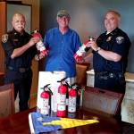 Eagle Harbor Yacht Club Vice Commodore Terry Kerby (center) presents fire extinguishers to Fire Chief Hank Teran and Police Chief Matt Hamner. (Photo courtesy of the Eagle Harbor Yacht Club)