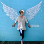 Port Orchard artist Gretchen Lund stands in front of the wing mural she painted on the wall outside Plum in downtown Winslow. Plum owner Theresa Collier said the mural, which was finished last week, is part of her efforts to lift spirits in the community during the COVID-19 outbreak. (Gabrielle Lund photo)