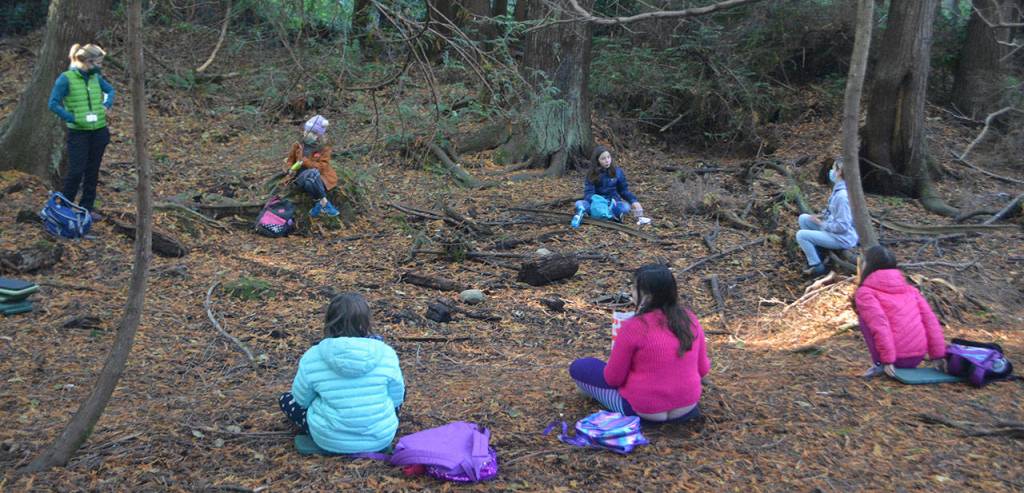 An IslandWood instructor talks to a group of students about what they saw on a short hike.
