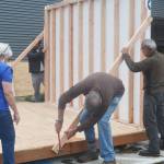 Volunteers hammer in a brace to give the first wall up in place.
