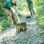 Benjamin Logan uses a rake to level out rocks on a trail.
