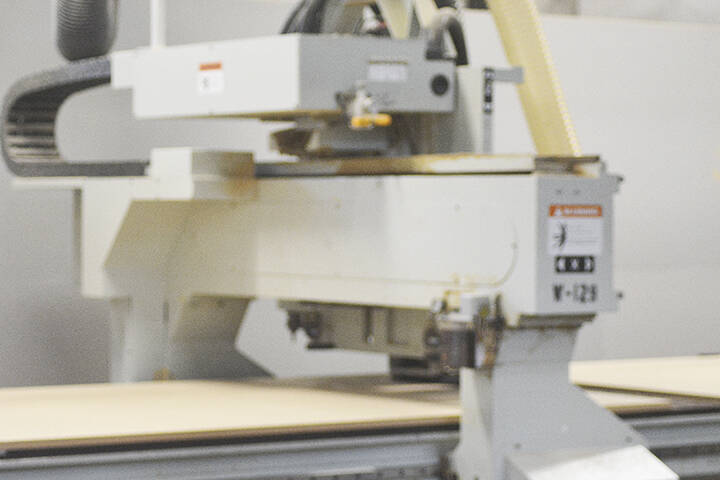 A router run by a computer makes cuts on a long piece of wood.