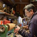 Carpenter Mike Okano shapes a kine from a cherry wood log on his lathe.