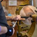 Wood shavings fly as a BARN member carves using a lathe in the wood shop.
