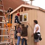 Student pointing out where the first nail should be placed to secure siding to the tiny house.