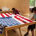 Deborah Ruddnick, right, and Naomi Spinak, left, embroider more than 100 names onto the white stripes of the flag quilt dedicated to victims of mass shootings in the United States. Courtesy photo