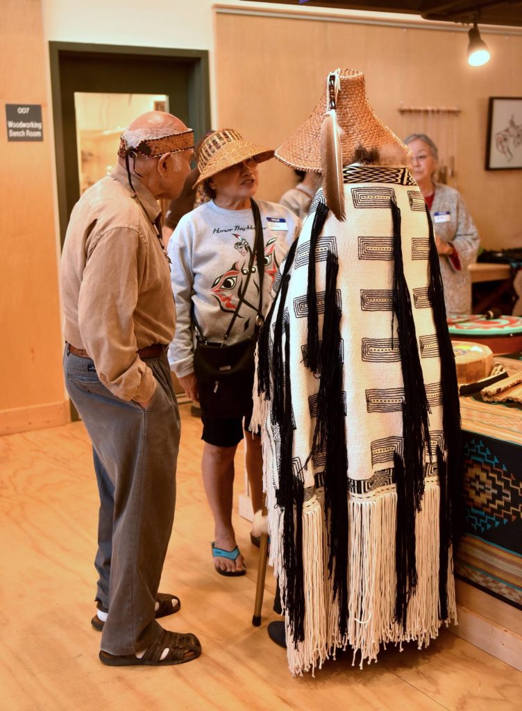 Ed Carriere, left, and Darlene Peters, wearing the black and white shawl she wove, speak with visitors.
