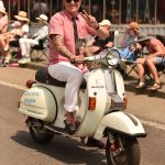 A Vespa driver waves at the crowd.